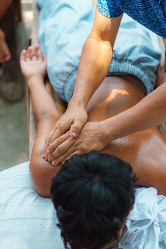 A relaxing outdoor massage session focusing on the arm and shoulder with natural light.