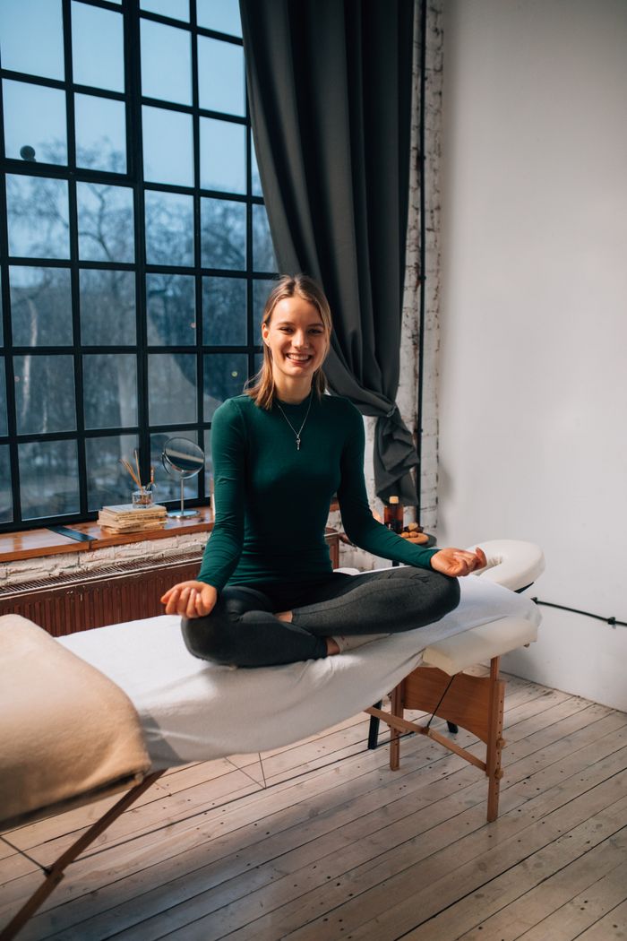 Woman in meditation pose on massage table, serene indoor setting, natural light.