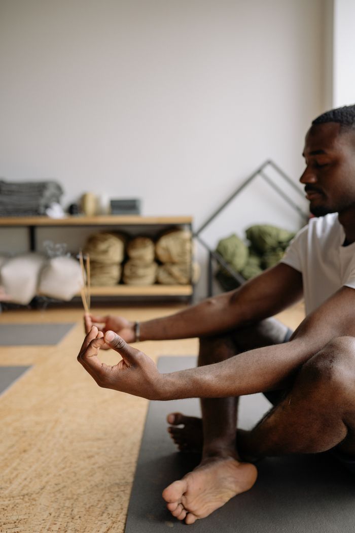 A man practices meditation indoors holding incense sticks, creating a peaceful atmosphere.